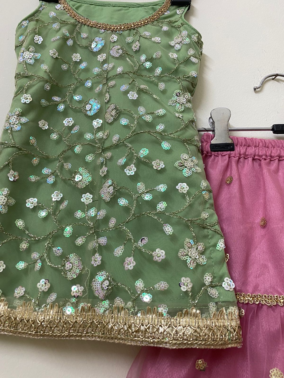 Green embroidered top with gold border and pink pants on a white background