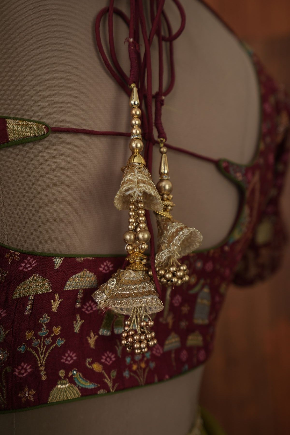 Open-back maroon blouse with decorative tassels paired with olive green saree