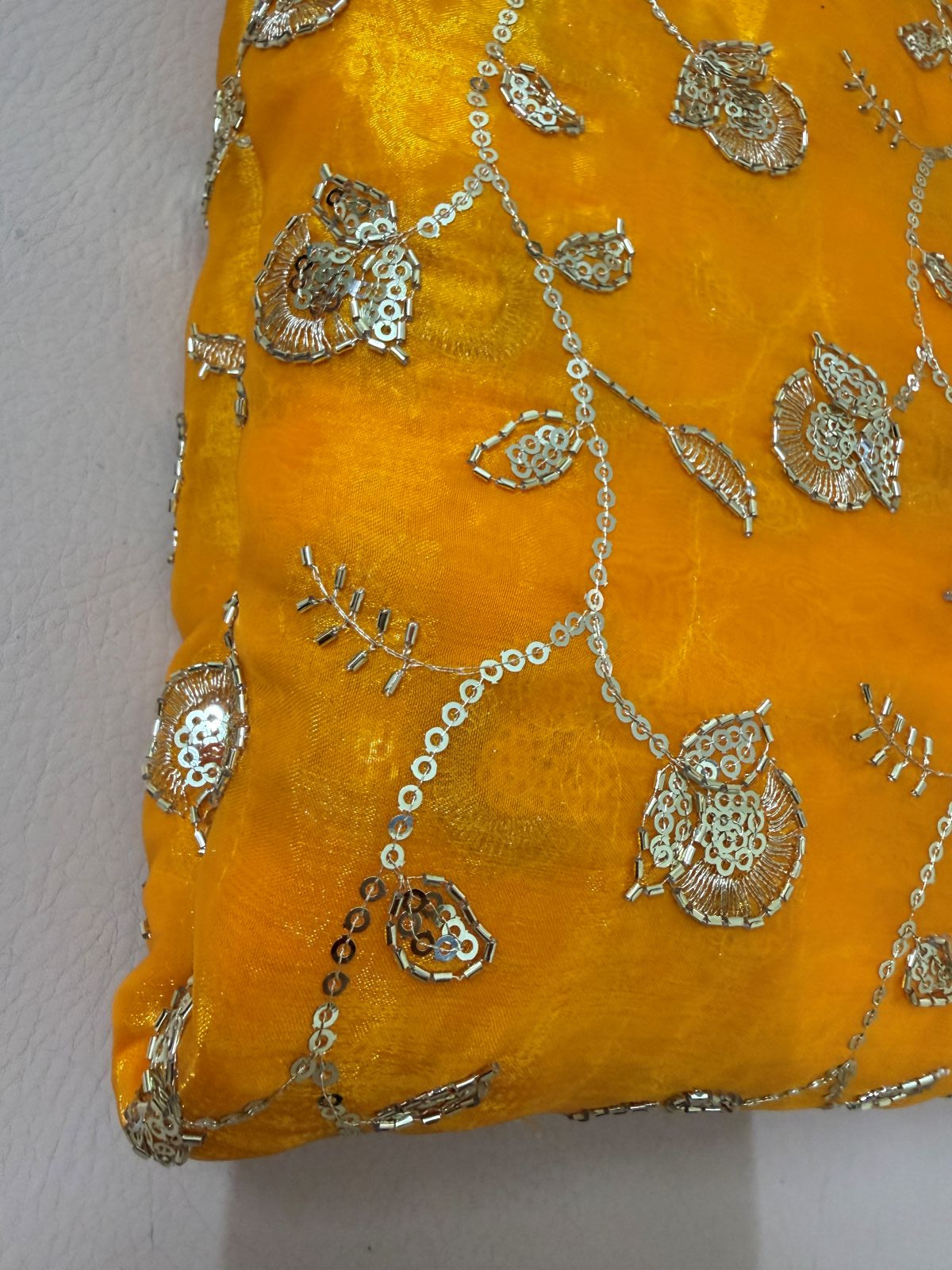 Close-up of mustard-gold lehenga skirt showing floral motifs, leafy details, and linked sequin-style embellishment