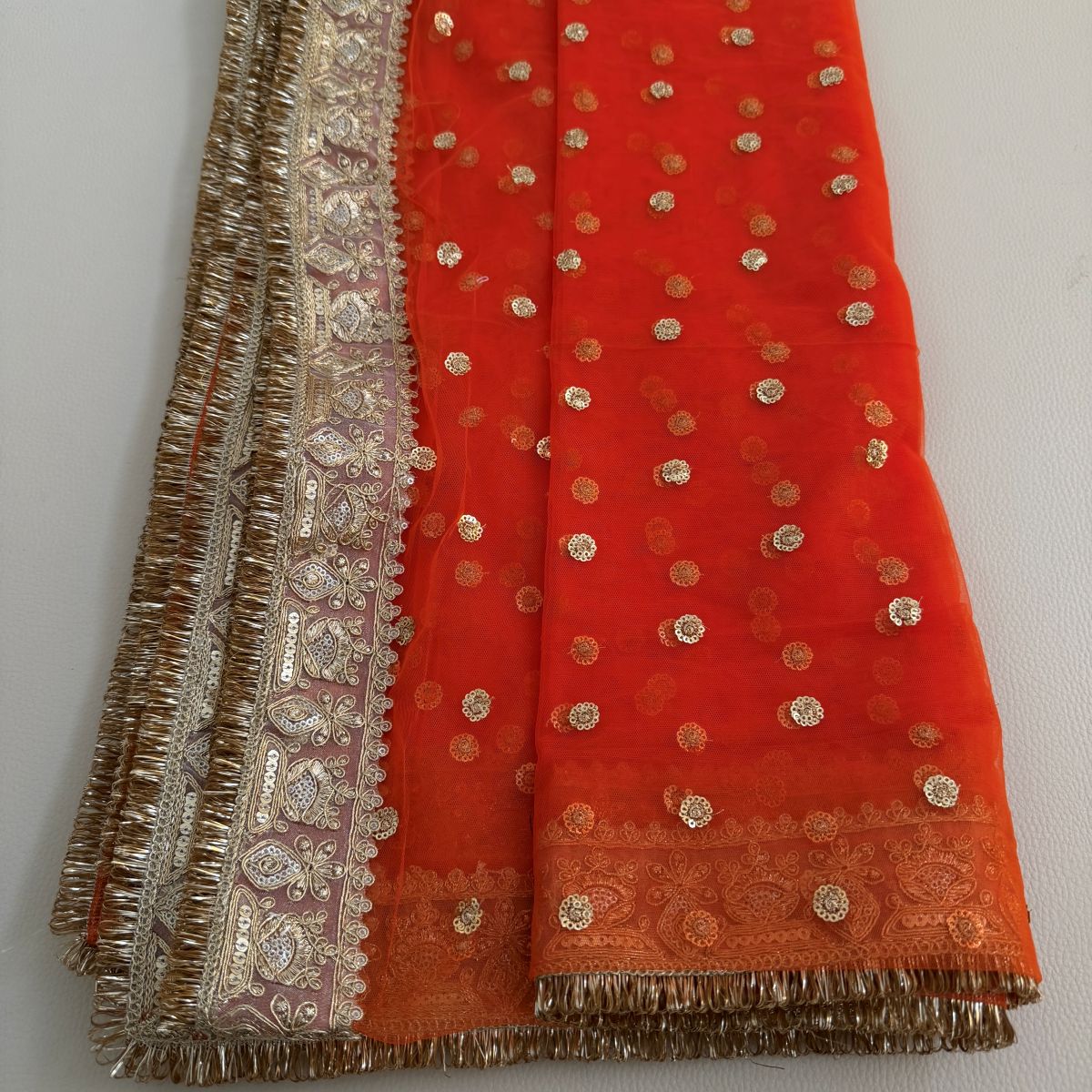 Close-up of orange dupatta with ornate floral border and fringe edging