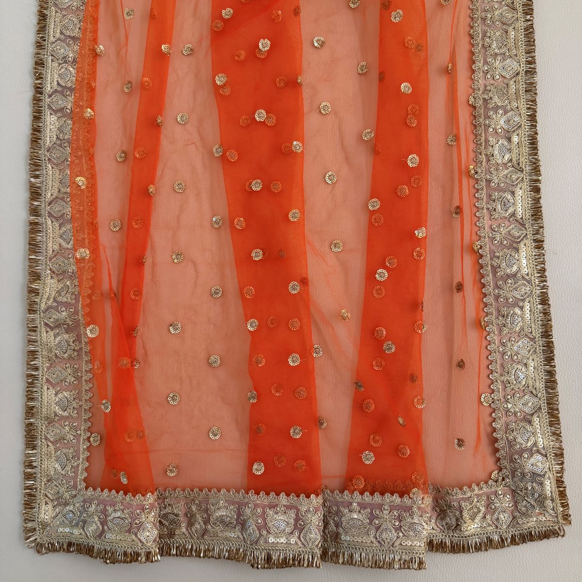 Folded orange dupatta showing gold motifs and ornate border