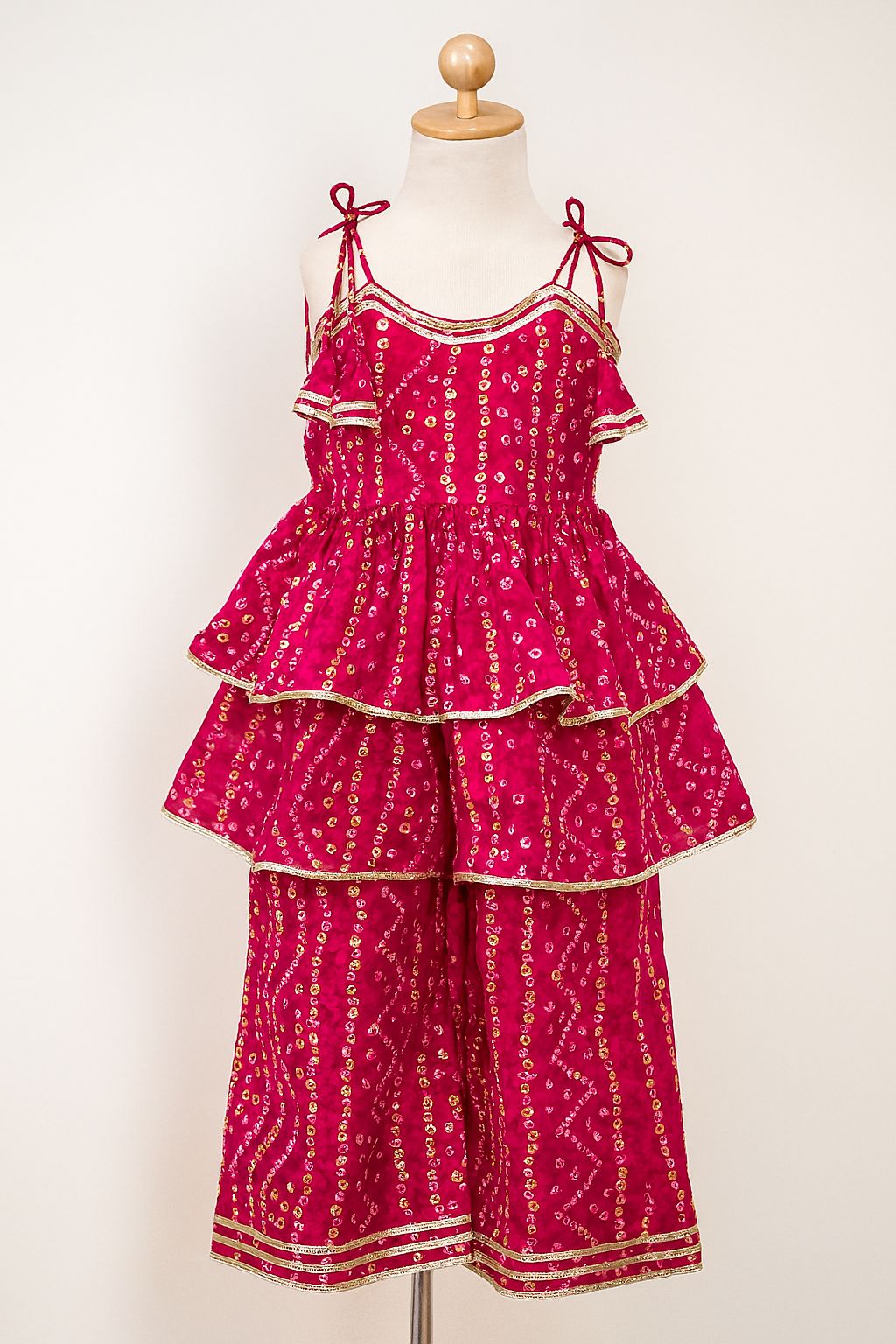 Pink tiered dress with gold patterns on a mannequin against a white background