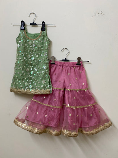 Green top and pink skirt with gold details on hangers against a white wall.